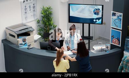 Secrétaire travaillant à la réception de l'hôpital pour aider les patients à se rendre à l'examen dans la salle d'attente. Réceptionniste qui donne des rapports médicaux à un groupe de personnes dans le hall de la clinique. Prise de vue à main levée. Banque D'Images