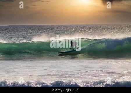 Un jeune surfeur a silhoueté en montant dans le tube de Maui au coucher du soleil. Banque D'Images