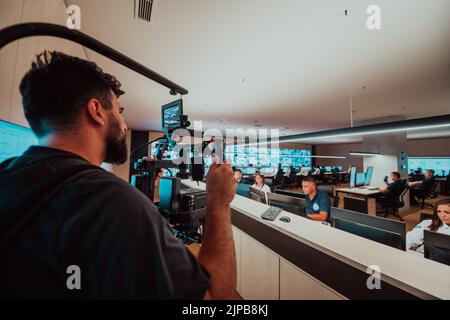 Vidéaste professionnel avec vidéo slr de gimball enregistrant la vidéo des opérateurs de centre de données de sécurité tout en travaillant dans une salle de surveillance de CCTV regardant Banque D'Images