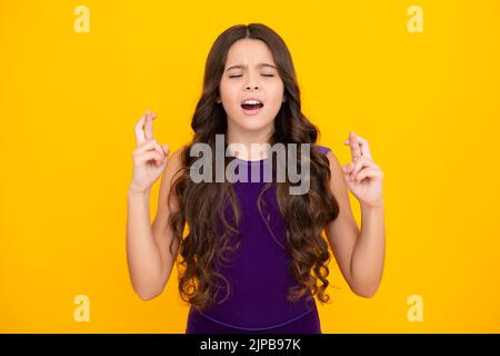 Un adolescent tenant les doigts croisés pour Bonne chance. La jeune fille prie et espère que les rêves deviennent vrais, isolé sur fond jaune. Banque D'Images