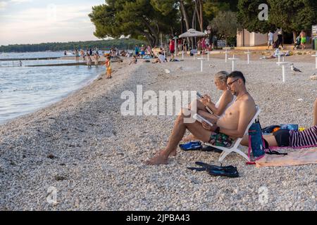 Un couple lisant des livres tout en se reposant sur une plage de sable lors d'une belle journée d'été Banque D'Images