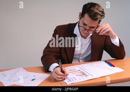 Homme d'affaires qui passe en revue les tableaux importants. Responsable d'entreprise travaillant à son bureau pour analyser les données. Analyste de données. Homme blond habillé d'un costume et de lunettes. Photo de haute qualité Banque D'Images