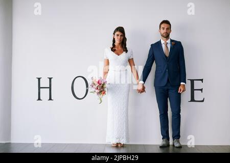 Quand deux deviennent un. Concept studio portrait d'une mariée et marié faisant un M dans le mot maison contre un mur. Banque D'Images