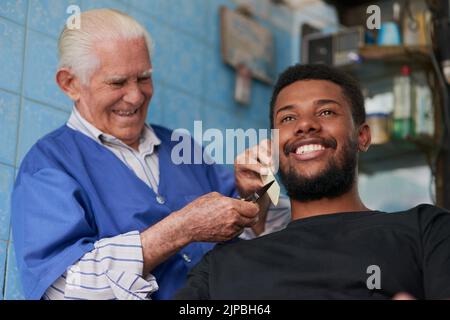 Toujours perfectionniste quand il s'agit de ses clients. Un homme âgé tailler la barbe d'un client dans son salon de coiffure. Banque D'Images