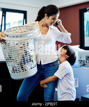 Il suffit d'attendre miel, IM au téléphone. Une jeune mère attrayante faisant la lessive avec son fils à la maison. Banque D'Images