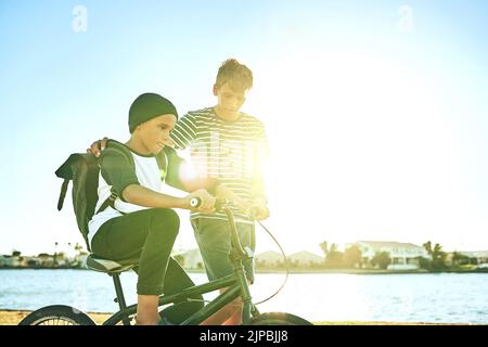 C'est ce que font les frères plus âgés. Un jeune garçon enseignant à son frère cadet comment faire un vélo le long d'un lagon. Banque D'Images