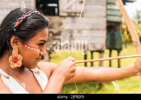 Une adolescente indigène avec un visage peint et des flèches de tir avec un arc en bois dans une communauté du nord des Caraïbes au Nicaragua. Banque D'Images