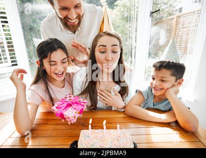 Anniversaire, famille et célébration avec une femme soufflant les bougies sur son gâteau. Mari et enfants gâtant maman et la rendant heureuse sur son spécial Banque D'Images