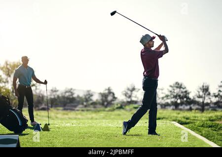 Bien joué. Un jeune golfeur masculin concentré sur le point de balancer et de jouer un tir avec son club de golf à l'extérieur sur un terrain. Banque D'Images