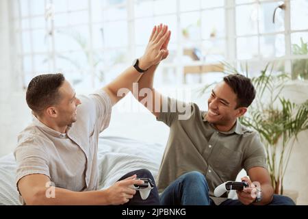 Les hommes en haut cinq, fêtez et profitez de jeux vidéo dans le canapé à la maison. Heureux, gai et meilleurs amis s'amusant et gagnant tout en tenant Banque D'Images