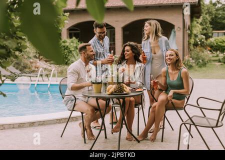 Groupe de jeunes heureux qui applaudissent au cidre près de la piscine dans le jardin Banque D'Images