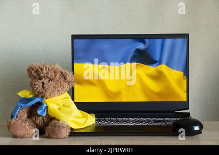 Le drapeau national de l'Ukraine comme arrière-plan sur un ordinateur portable et un ours en peluche se trouve à la maison à côté du drapeau de l'Ukraine sur la table. Arrêter la guerre, patriote Banque D'Images