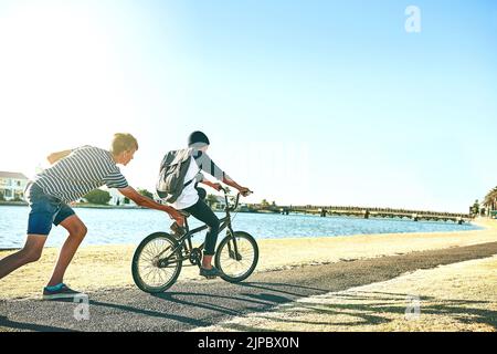 Un jeune garçon qui lui donne un peu de pression et apprend à son frère cadet à faire du vélo le long d'un lagon. Banque D'Images