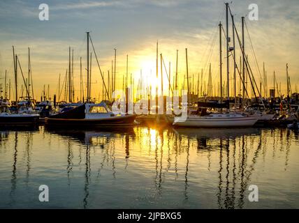 Soleil levant sur la marina de yarmouth sur l'île de wight, avec les reflets des bateaux dans l'eau Banque D'Images