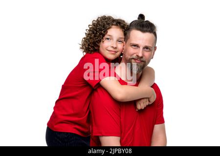 Beau père seul tenant un porcgyback adorable fille de 10-12s. Femme enfant fille embrassée avec amour papa barbu. Famille sympa vêtements de base rouge t- Banque D'Images