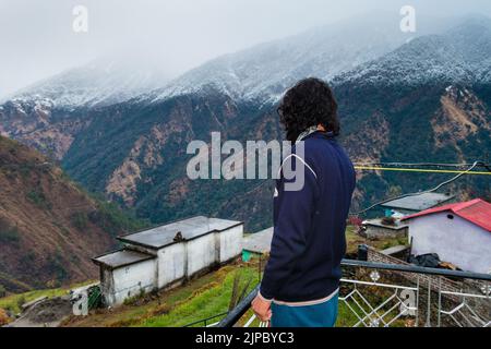 Uttarakhand. Inde. 23rd Jan2022.A Homme debout sur le toit d'une maison de village avec des montagnes couvertes de neige de l'himalaya dans le district d'Okhimath de Cha Banque D'Images