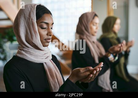 Priant, des groupes de femmes musulmanes et jeunes pratiquant la religion arabe, sainte et islamique à l'intérieur. Les femmes portant un hijab tout en s'agenouillant pour pratiquer un calme Banque D'Images