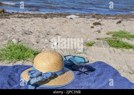 Chapeau de paille, lunettes de soleil et tongs sur une serviette bleue sur une plage naturelle au bord de la mer, près de la station touristique Boltenhagen, mer Baltique, Allemagne, sélectionné Banque D'Images