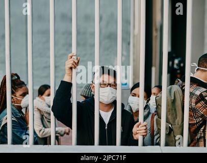 Derrière les barreaux, le verrouillage et les restrictions de covid avec un homme portant un masque pendant une pandémie et l'interdiction de voyager. Portrait d'un homme enfermé pendant Banque D'Images