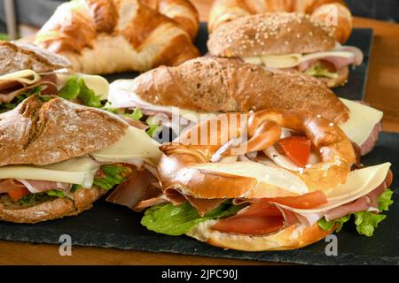 Grand choix de sandwichs appétissants avec fromage au jambon et légumes servis sur des planches d'ardoise sur une table en bois au restaurant Banque D'Images