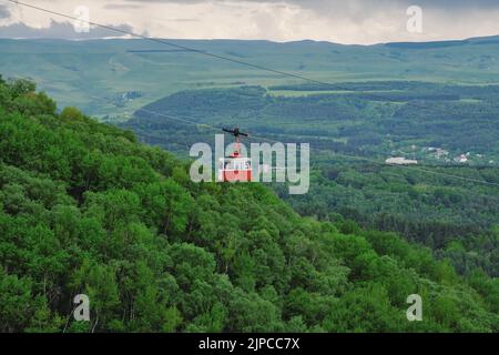 Cabine rouge du téléphérique au-dessus de la forêt. Cabine de funiculaire au-dessus des collines verdoyantes. Parc national de Kislovodsk, Russie. Banque D'Images