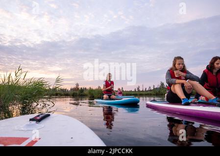 Jeunes sur un panneau SUP nageant sur le lac en regardant le lever du soleil. Banque D'Images