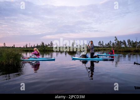 Jeunes sur un panneau SUP nageant sur le lac en regardant le lever du soleil. Banque D'Images