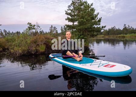 Jeunes sur un panneau SUP nageant sur le lac en regardant le lever du soleil. Banque D'Images