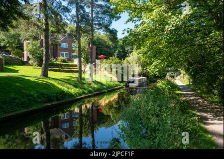 Le bateau à Narrowboat amarré sur le canal du Caldon dans le Staffordshire sous un soleil éclatant parmi les arbres et les arbustes. Banque D'Images