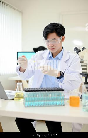 Portrait, Smart et beau jeune asiatique scientifique ou chercheur médical utilisant un tube compte-gouttes pour ajuster l'échantillon sur une boîte de Petri dans la moderne la Banque D'Images