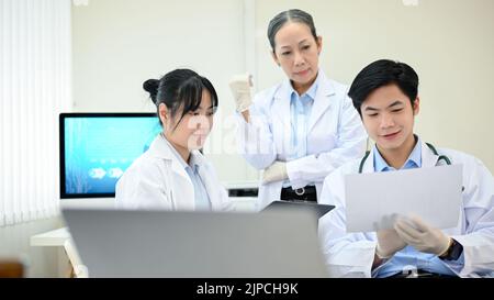 Deux jeunes scientifiques asiatiques ou techniciens médicaux travaillant, ayant une réunion de discussion médicale avec une femme asiatique supérieure superviseur scientifique dans le labo Banque D'Images