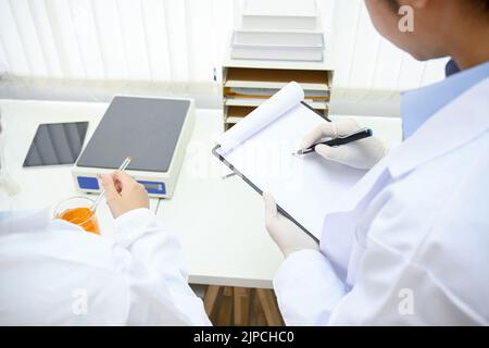 Un scientifique ou un technicien médical professionnel et intelligent travaillant dans son laboratoire de bureau enregistre un résultat d'expérience sur son presse-papiers Banque D'Images