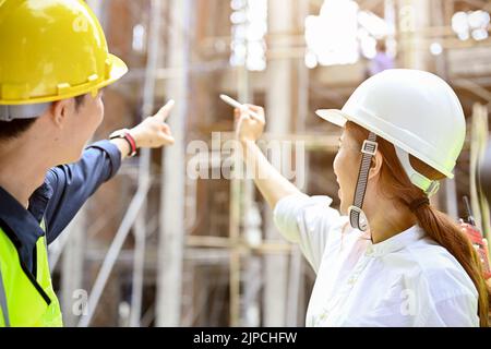 Une belle femme asiatique millénaire architecte en casque blanc, rencontre et planification d'un plan de construction avec un ingénieur professionnel au constr Banque D'Images