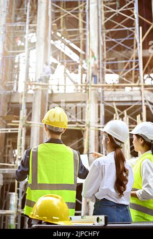 Une équipe d'ingénieur ou d'architecte asiatique professionnel et prospère dans le chantier de construction, regardant le bâtiment. Banque D'Images