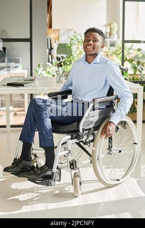 Portrait d'un jeune homme d'affaires africain assis en fauteuil roulant au bureau et souriant à la caméra Banque D'Images