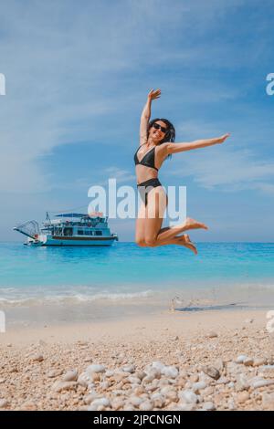 bonne femme souriante en maillot de bain noir sautant à la plage Banque D'Images