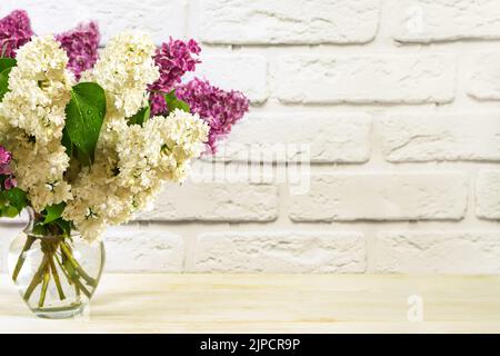 Belles fleurs de lilas violet et blanc en fleurs dans un vase sur fond de brique blanche murale. Composition florale. Fête des femmes, fête des mères, anniversaire et mariage Banque D'Images