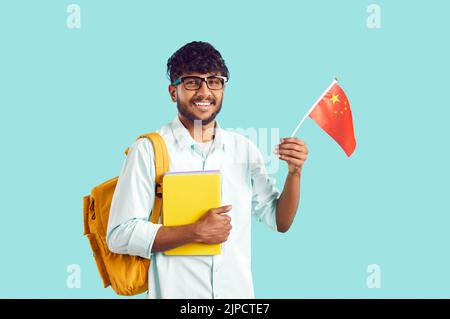 Joyeux étudiant indien avec sac à dos sur fond bleu clair avec drapeau chinois dans les mains. Banque D'Images