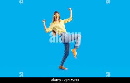 Joyeuse fille réussie de l'adolescence se réjouit et danses isolées sur fond bleu clair. Banque D'Images