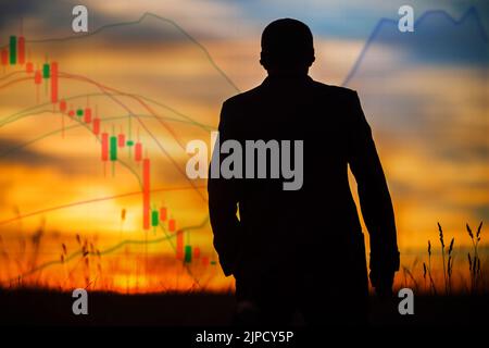 Silhouette d'un homme regardant les cartes du marché boursier au coucher du soleil. Investisseur professionnel, commerçant. Nouvelle crise financière économique à venir. Manipulateur de marché Banque D'Images