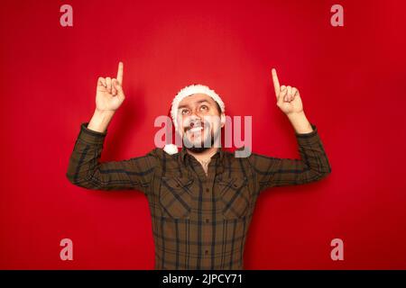 Portrait de l'homme souriant dans le chapeau de Noël vêtements décontractés pointant ses index vers le haut à l'espace vide Banque D'Images