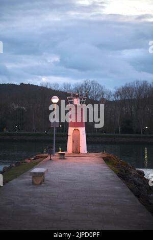 petit phare sur la jetée du port au crépuscule. Banque D'Images