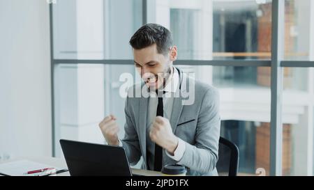 Jeune homme d'affaires utilisant un ordinateur portable recevoir de bons messages et devenir très excité et heureux s'assoit dans le bureau moderne à l'intérieur Banque D'Images