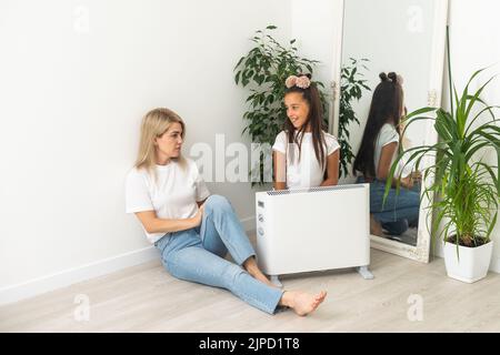 Chauffage électrique à la maison. Une jeune famille réchauffe ses mains gelées près d'un radiateur de chauffage Banque D'Images