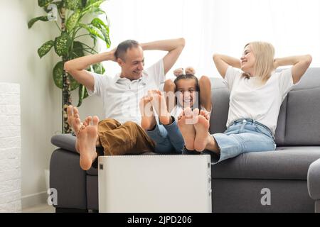 Chauffage électrique à la maison. Une jeune famille réchauffe ses mains gelées près d'un radiateur de chauffage Banque D'Images