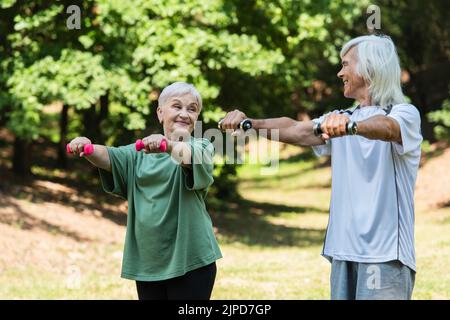 un couple positif à la retraite dans les sports s'exerçant avec des haltères dans le parc vert Banque D'Images