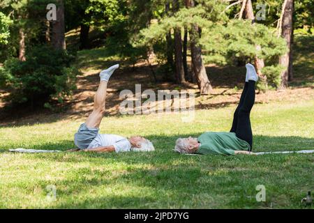 longueur totale d'un couple senior dans des vêtements de sport faisant une épaule sur des tapis de fitness dans le parc vert Banque D'Images