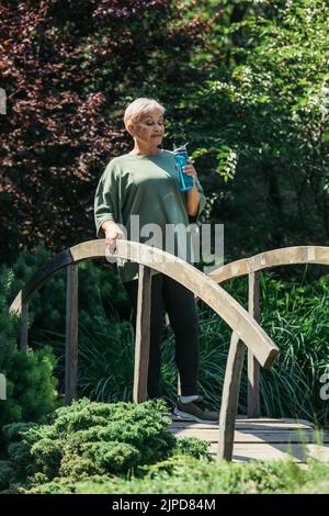 pleine longueur de femme sénior sportive tenant une bouteille de sport et debout sur le pont Banque D'Images