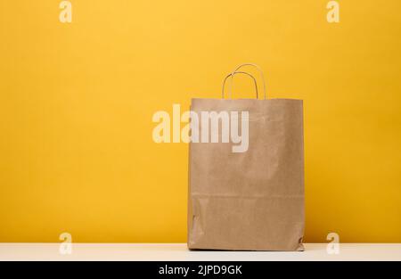 Un sac en papier marron se trouve sur une table blanche, sur fond jaune. Emballage du produit Banque D'Images