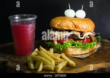 hamburger colombien avec pommes de terre et jus de fruits rouges, servi sur un plateau en bois en forme de tronc d'arbre. hamburger avec deux œufs de caille sur le dessus de l'imit Banque D'Images